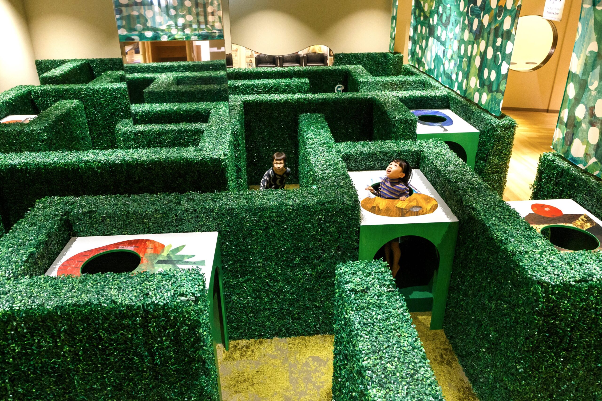 PLAY! PARK ERIC CARLE館内の緑の生垣で作られた迷路で遊ぶ子ども
