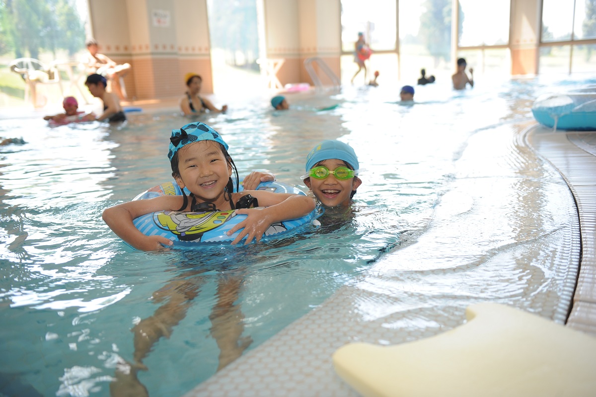 室内温水プールで浮き輪を使って泳ぐ子どもたち