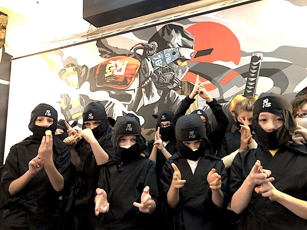 忍者衣装を着た参加者たちが壁画の前で並ぶ様子