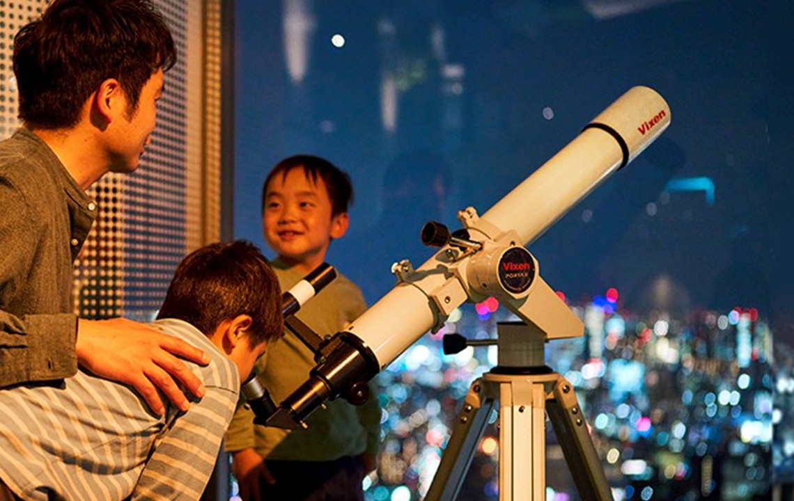 てんぼうパークの展望フロアで望遠鏡から夜景を眺める親子