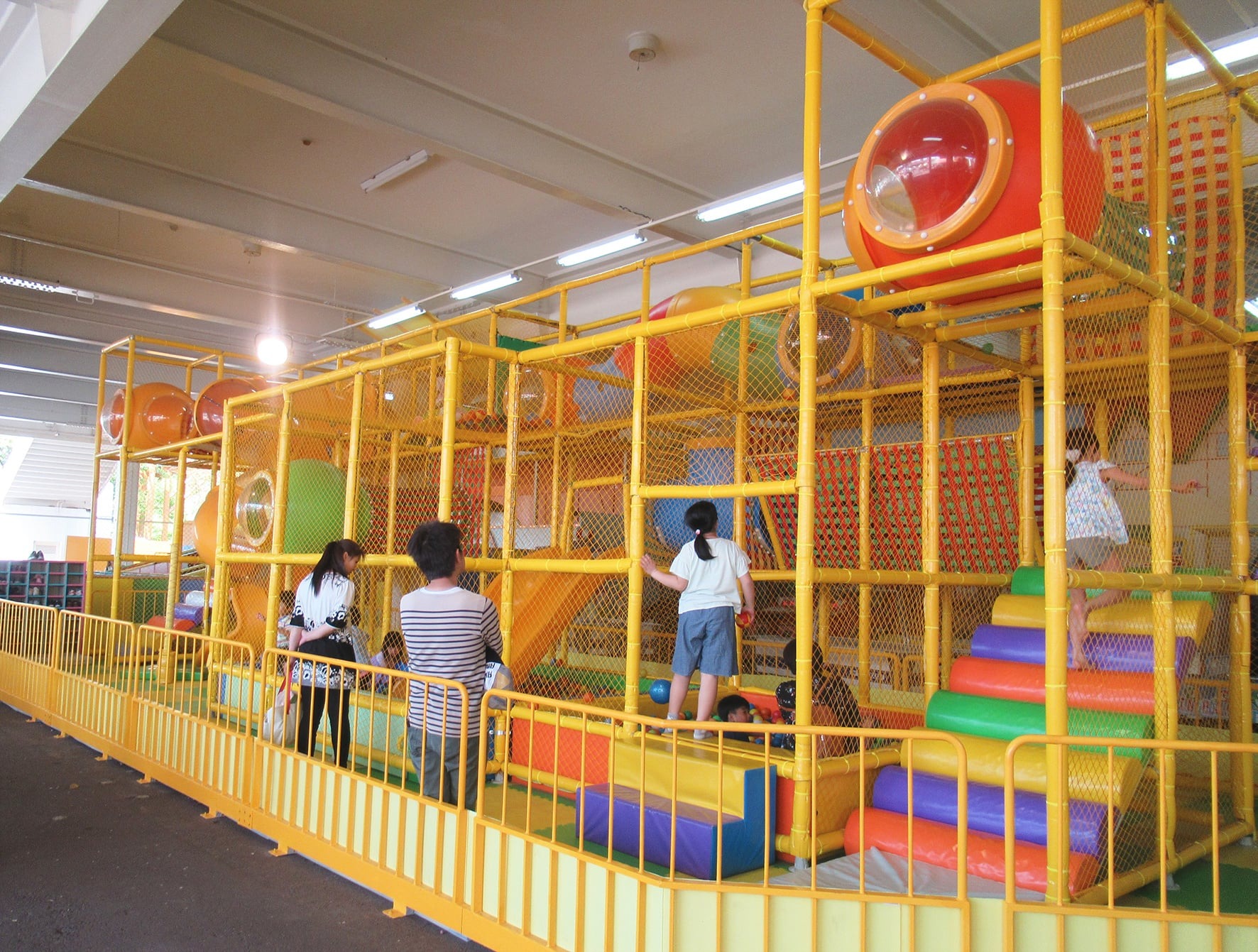屋根の下の黄色いパイプでできた立体遊具で遊ぶ子どもたち