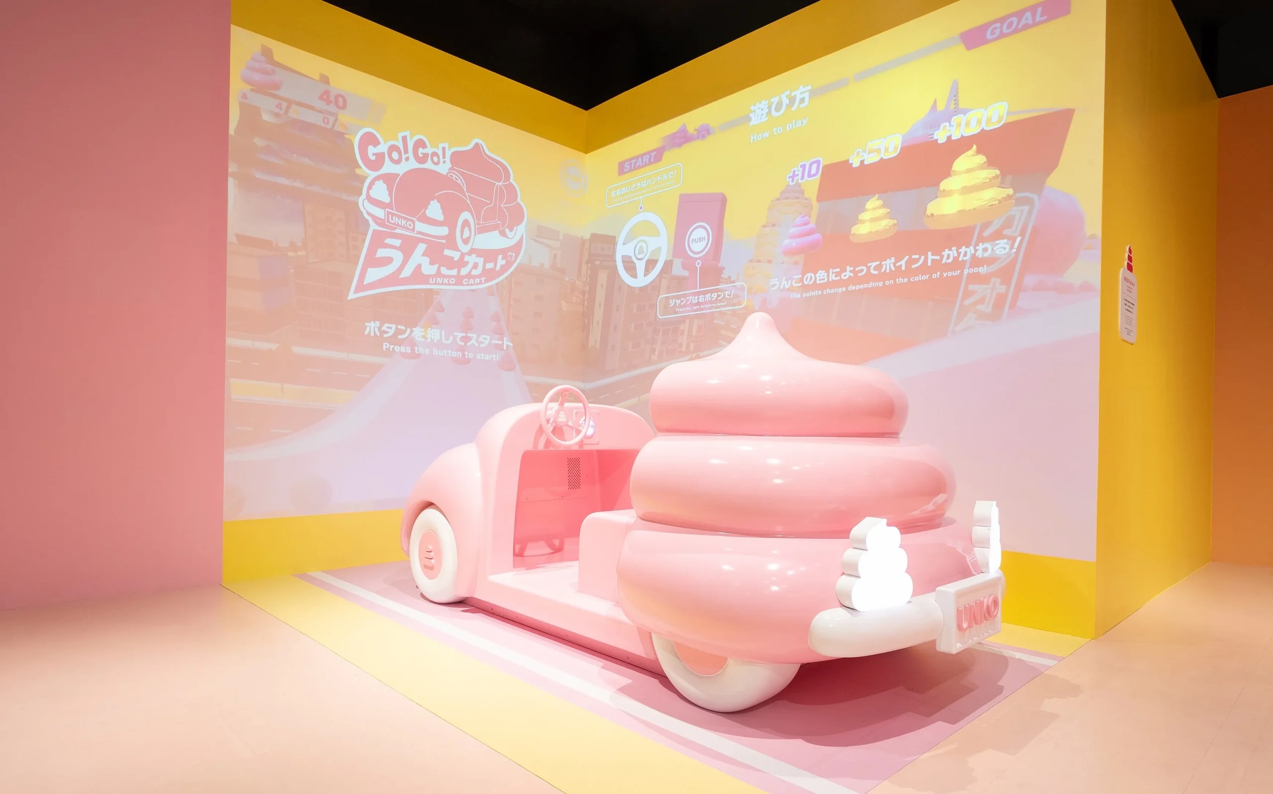 壁の映像の前に置かれたピンクのうんこ型カート(うんこミュージアム NAGOYA)