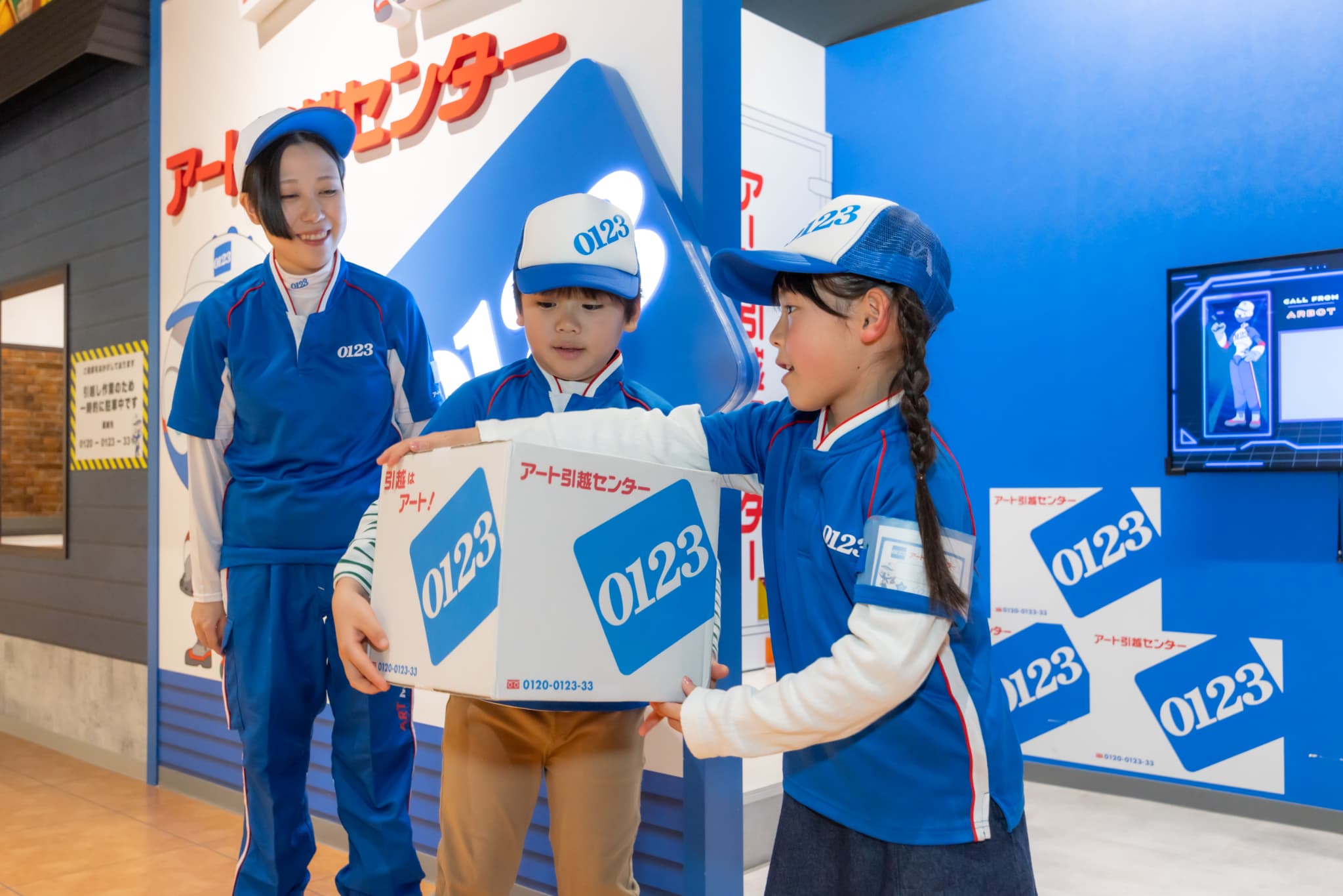 引越センターの青い制服と帽子でダンボールを運ぶ子どもたち(カンドゥー大日)