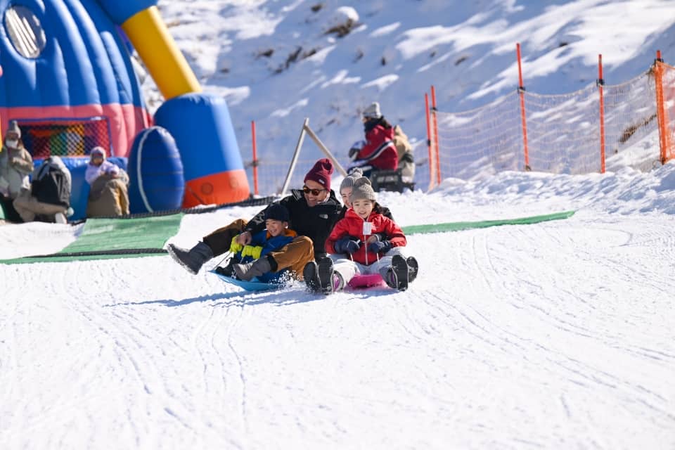 そりで雪の斜面を滑る親子とふわふわ遊具(佐久スキーガーデン パラダ)
