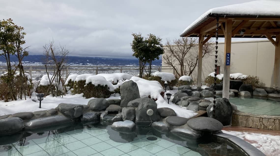 雪をかぶった岩に囲まれた露天風呂と山並み