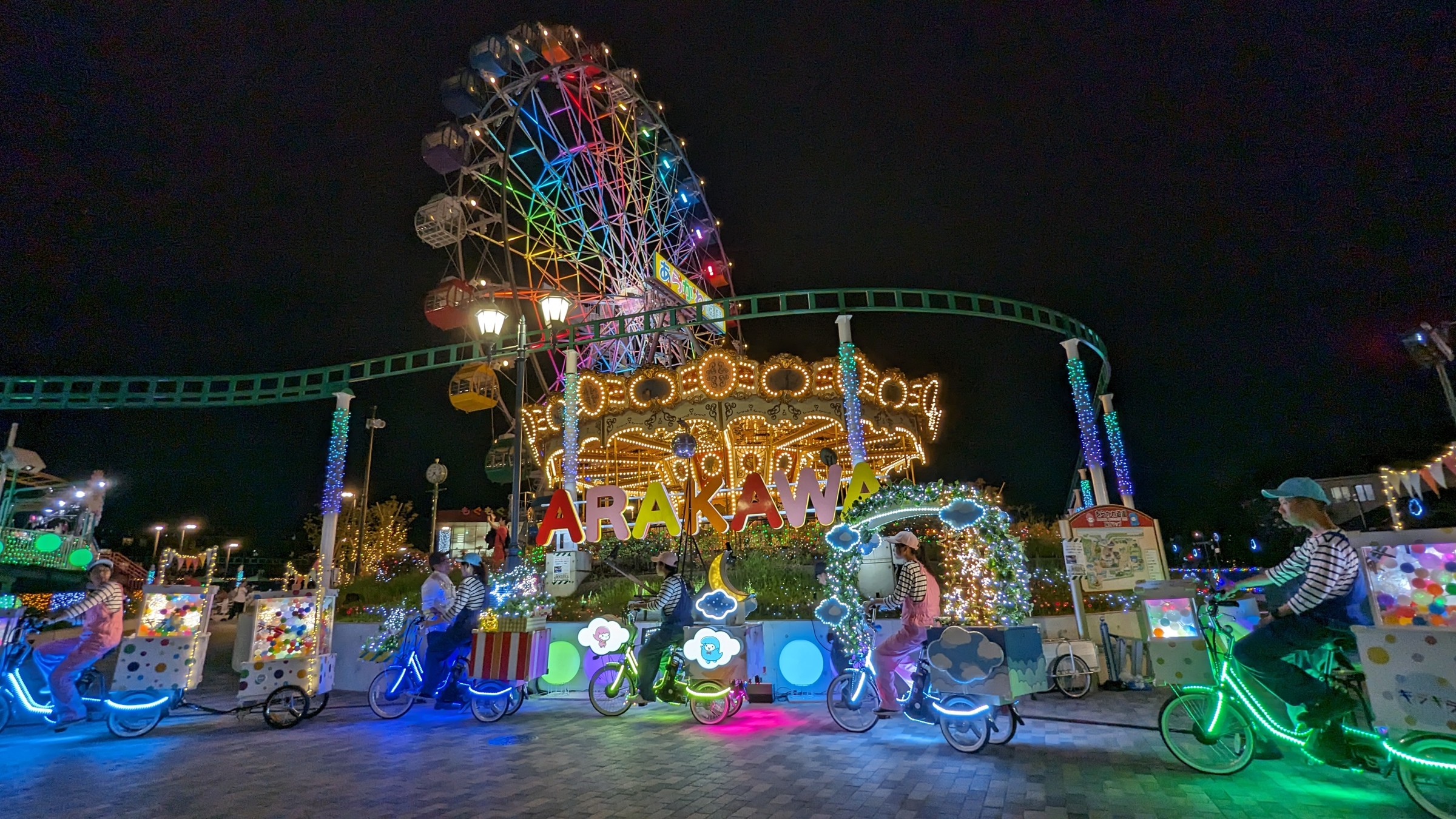 夜の観覧車の前を進む電飾の自転車パレード