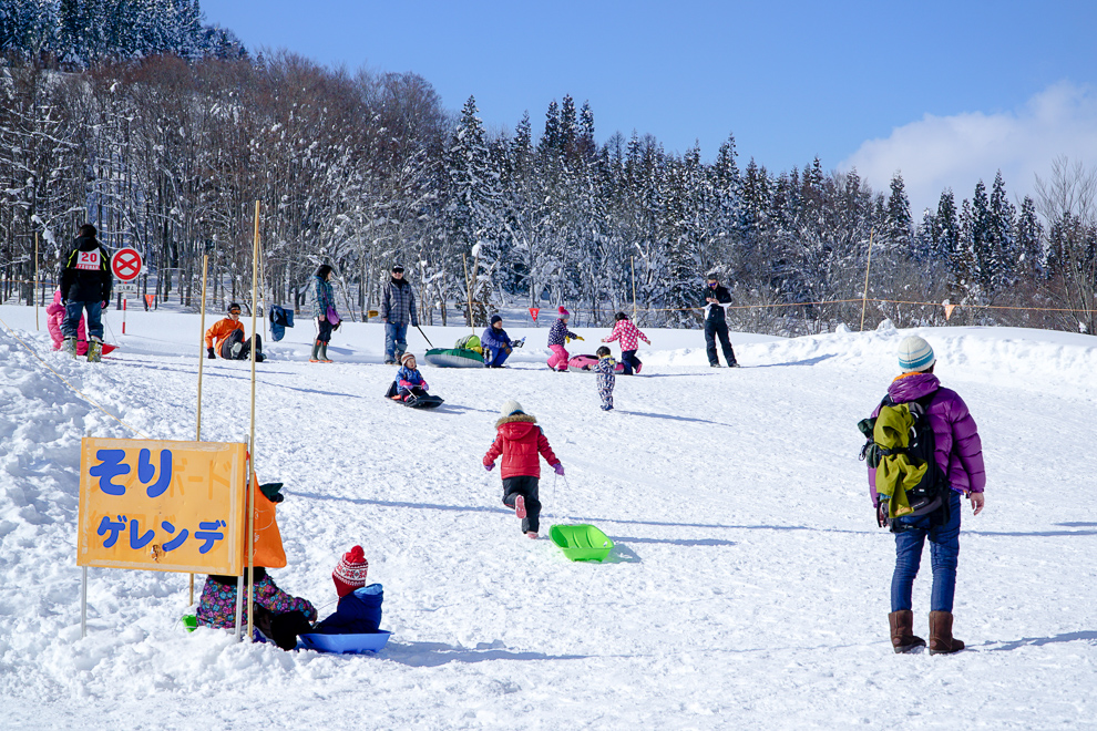 そりゲレンデの看板と雪遊びをする子どもたち
