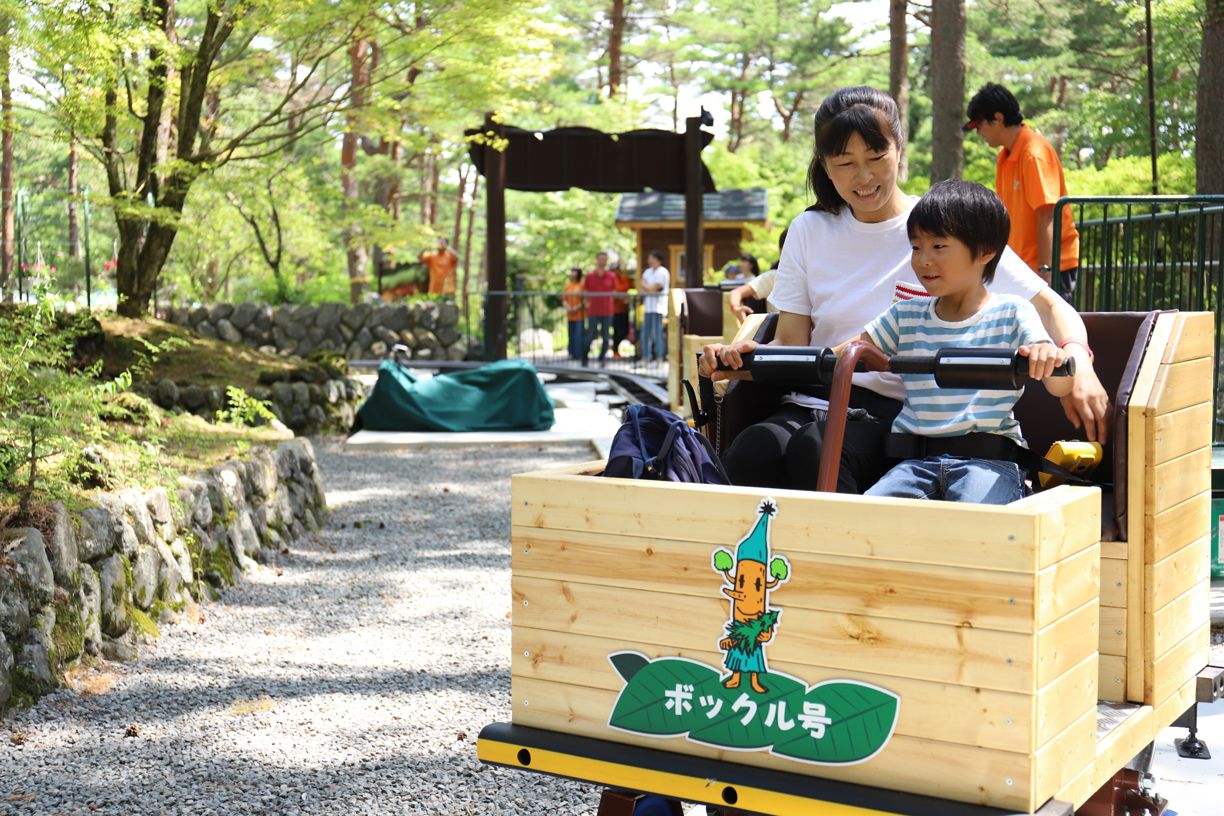木製のトロッコに乗る親子と森へ続く線路