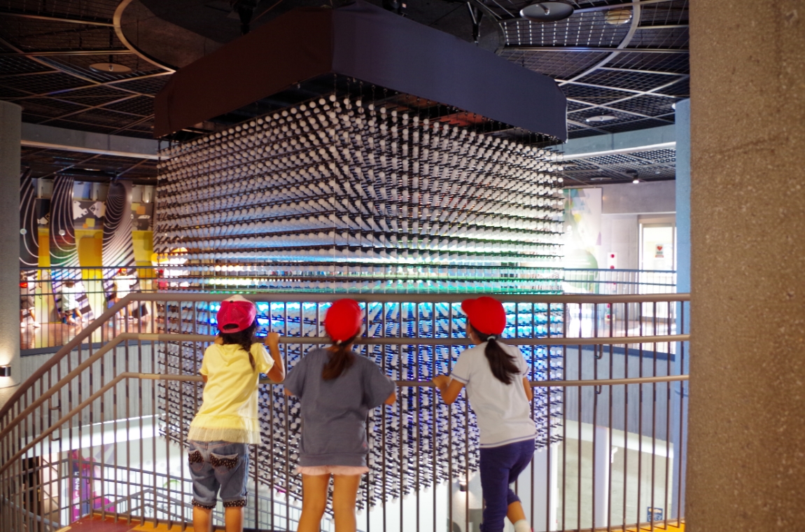 吹き抜けに吊られた大きな展示を見る子どもたち(沖縄こどもの国 ワンダーミュージアム)