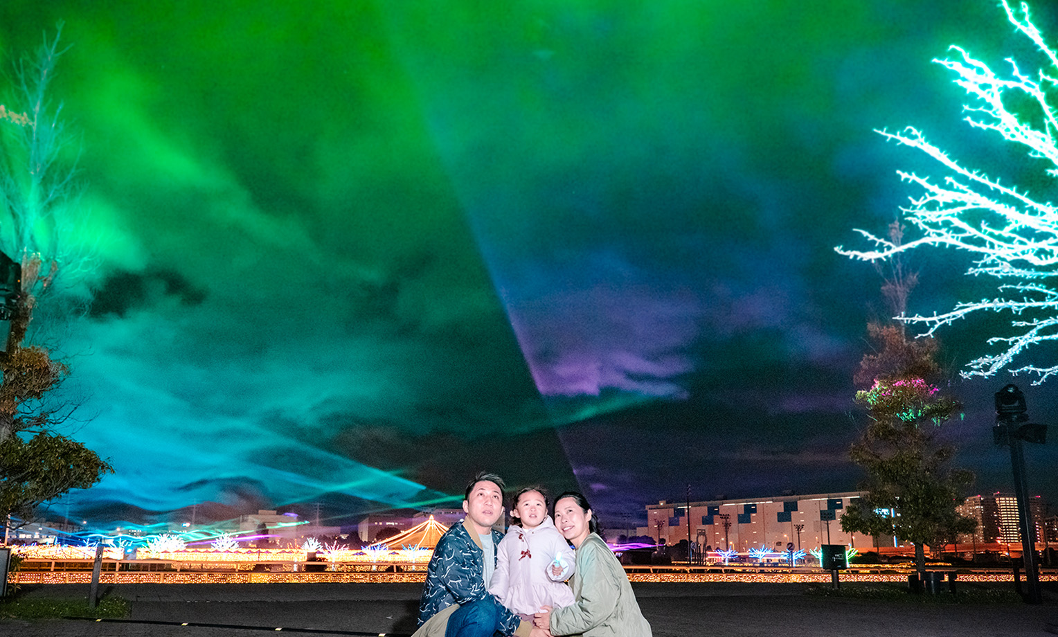 緑と紫のレーザーが夜空に広がるオーロラの森と見上げる親子
