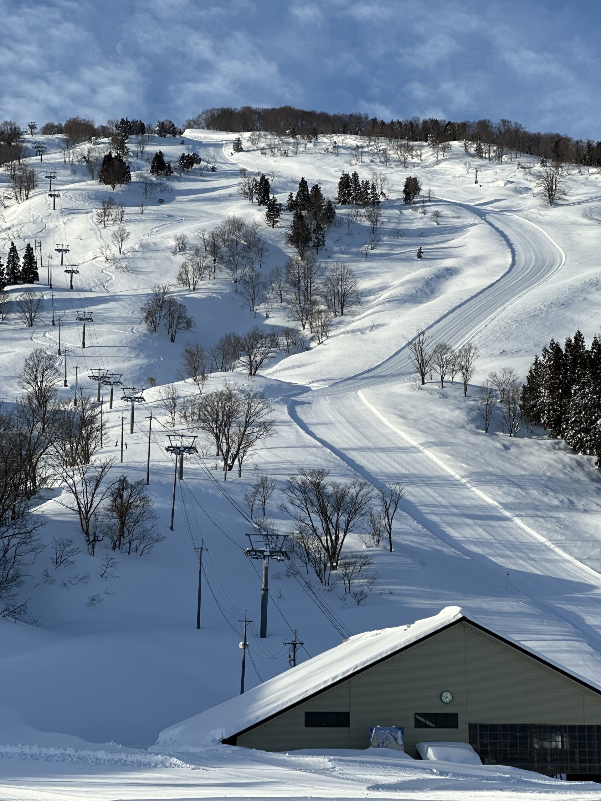 リフトの支柱が並ぶ横を圧雪コースが曲がりながら下りてくるゲレンデ