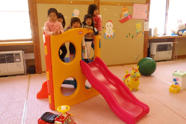 滑り台のある託児所の室内で遊ぶ子どもたち