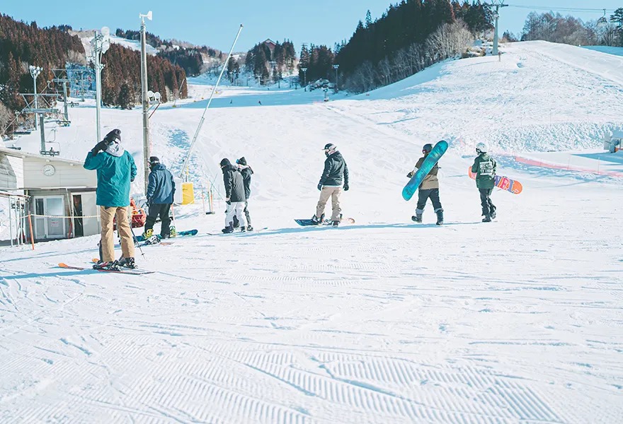 圧雪されたゲレンデの下を、スキーやスノーボードを持って歩く人たち
