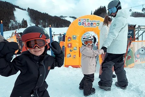KIDS GELENDEと書かれたオレンジ色の入口の前で遊ぶゴーグル姿の子どもたち
