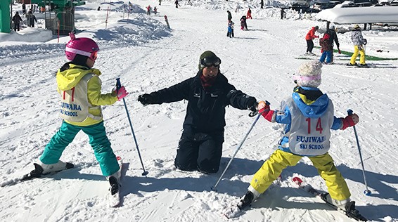 ゼッケンを付けた子ども2人にスキーを教えるコーチ