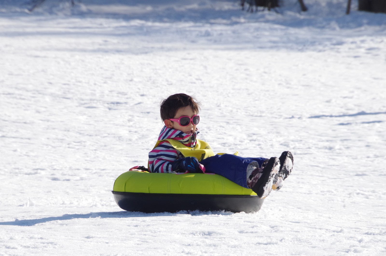 チューブに乗って雪の上をすべる子ども