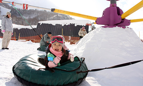 雪の山の上の回転遊具につながれたチューブに乗る女の子