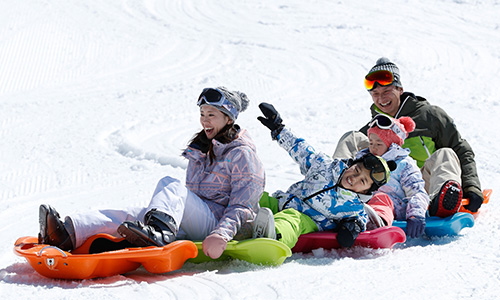 色とりどりのソリに並んで座り、雪の上で笑う家族4人