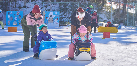 雪の上で乗り物の遊具に乗る小さな子どもと親