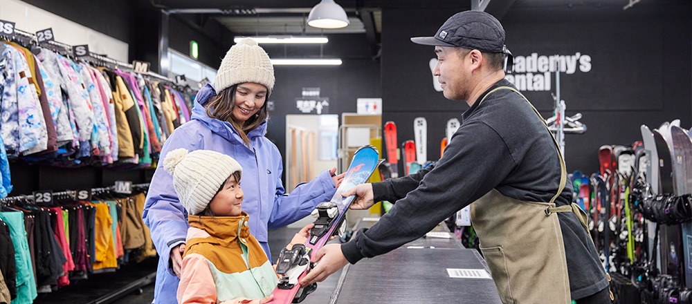 レンタルのカウンターでスキー板を受け取る親子