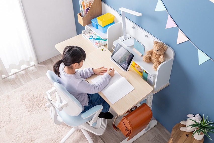高さを変えられる学習机で勉強する子ども