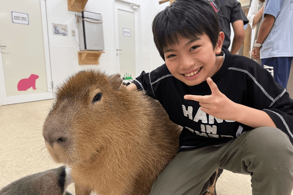 カピバラのとなりでポーズをとる男の子