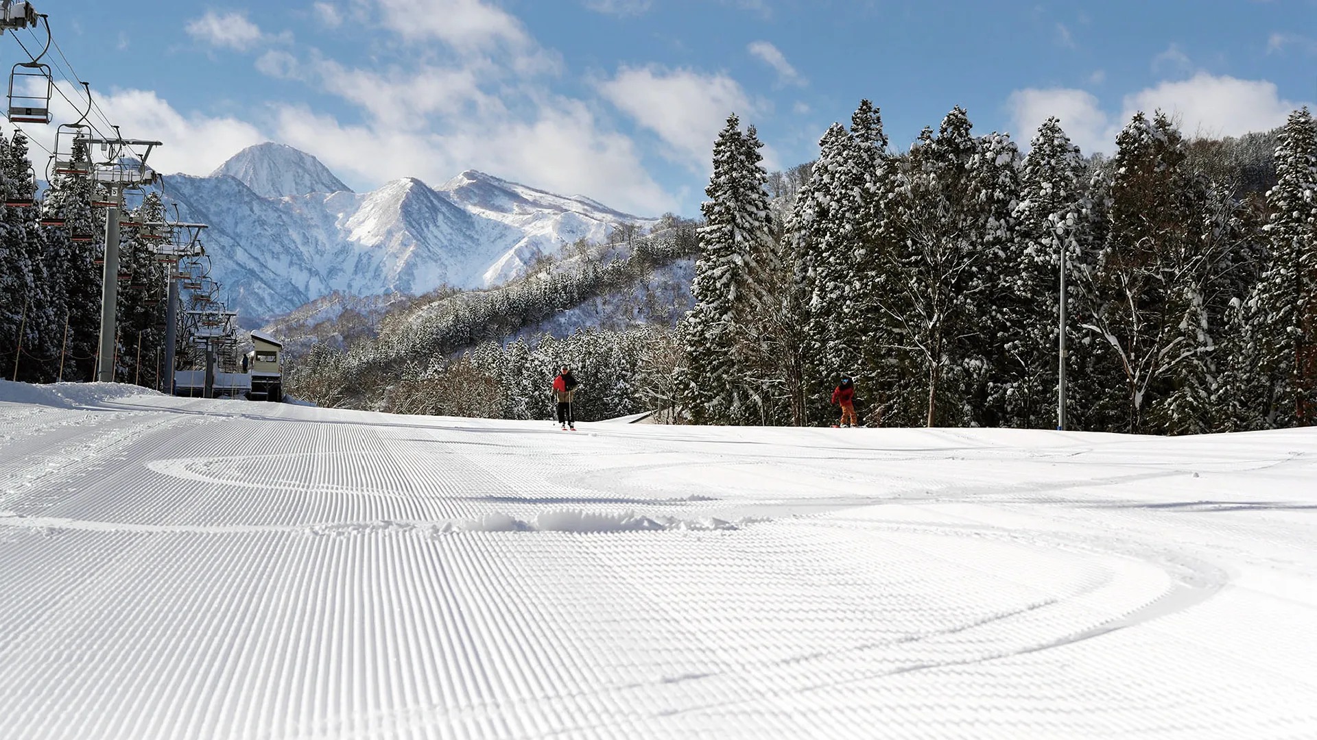 圧雪されたゲレンデと左手のリフト、奥の雪山