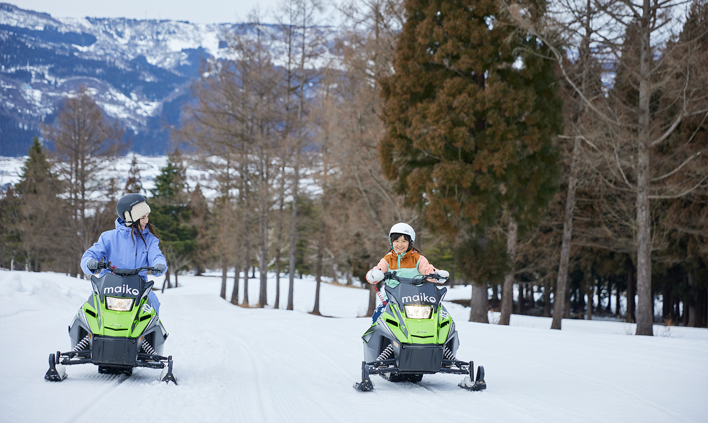 雪道で小型のスノーモービルに乗る大人と子ども